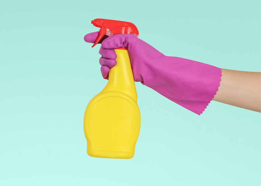 photo of person with pink rubber glove holding a yellow bottle of cleaner, in front of a blue background