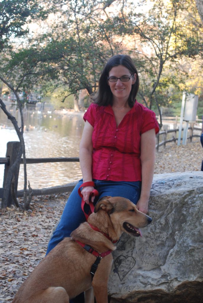 Photo of Beth Patton, massage therapist, with her dog, in front of a lake