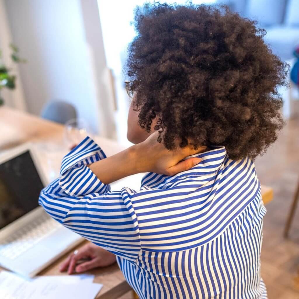 photo of woman working at her desk, holding her neck in pain.